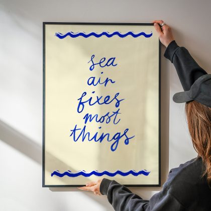 Sea Air Fixes Most Things. Hand painted words in blue naïve brush script on a cream background with wave shaped borders top and bottom.